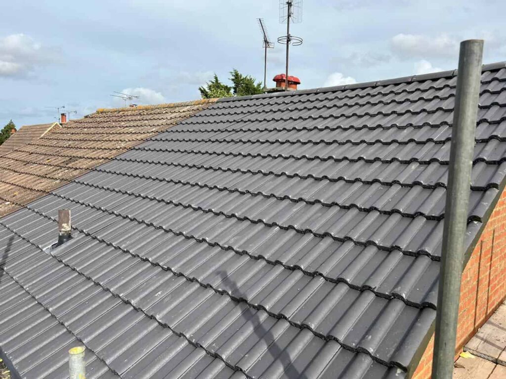 This is a photo of a newly constructed roof. The photo has been taken by the roofer who is standing on scaffold and it shows one side of the pitched roof and the chimney. Grey tiles have been installed on this roof.