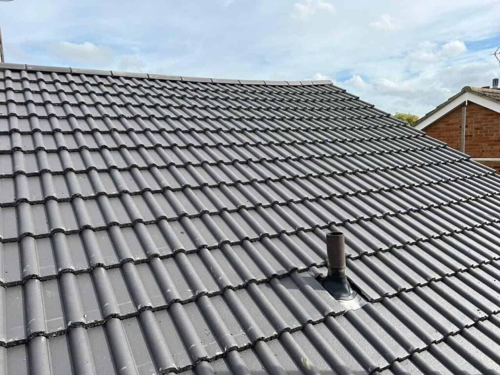 This is a photo of a newly constructed roof. The photo has been taken by the roofer who is standing on scaffold and it shows one side of the pitched roof. Grey tiles have been installed on this roof.