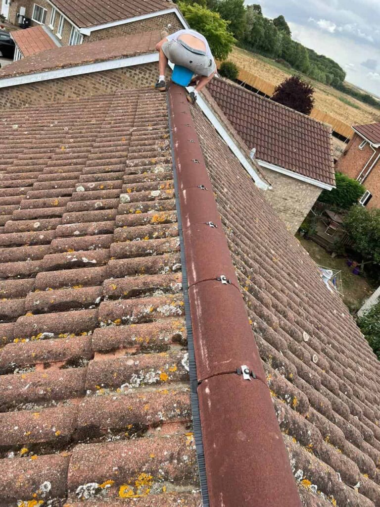 This is a photo of our roofer crouching on the roof ridge and installing new ridge tiles. He is cementing the final ridge tile in place.